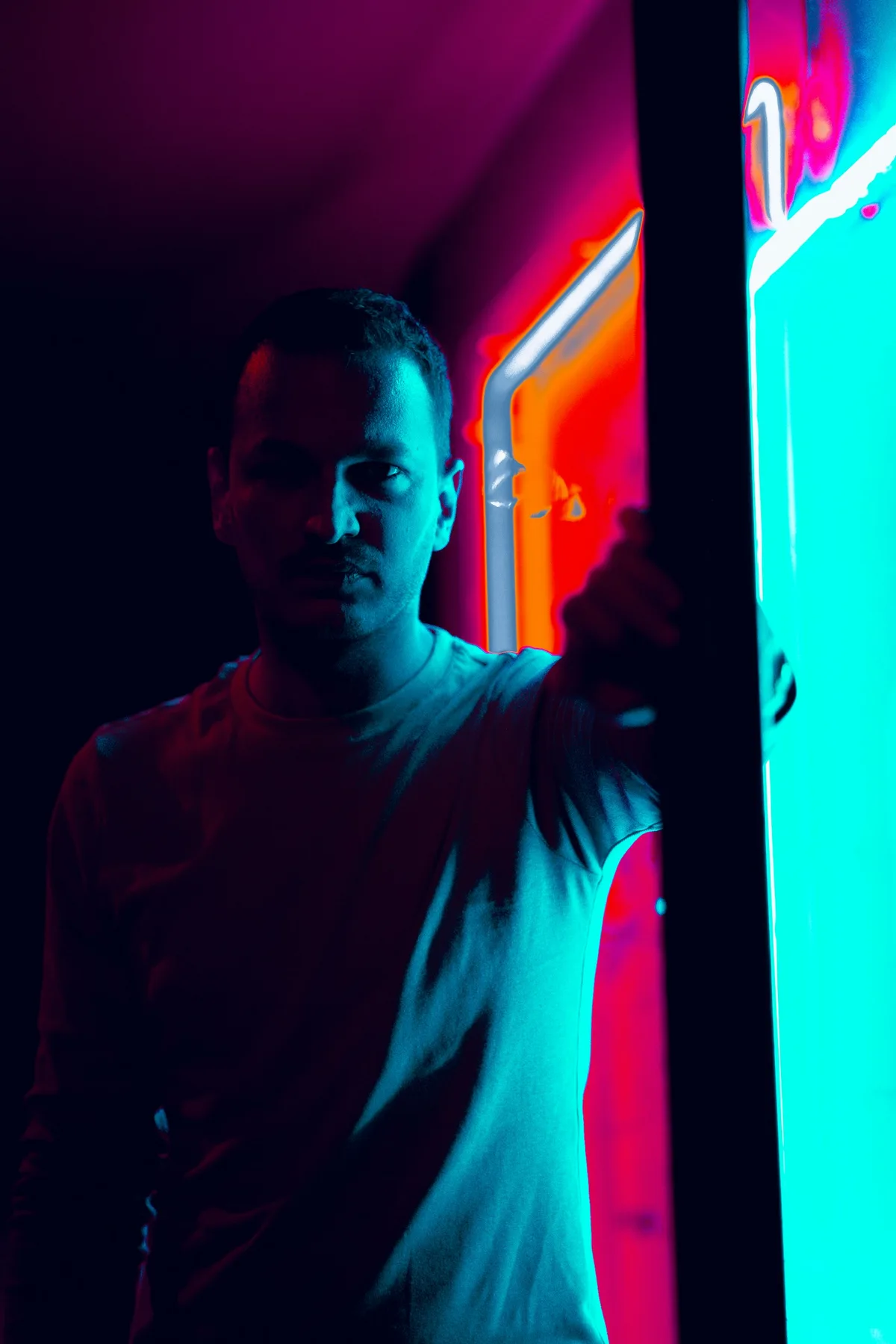 Person standing under teal and red neon signage at night.