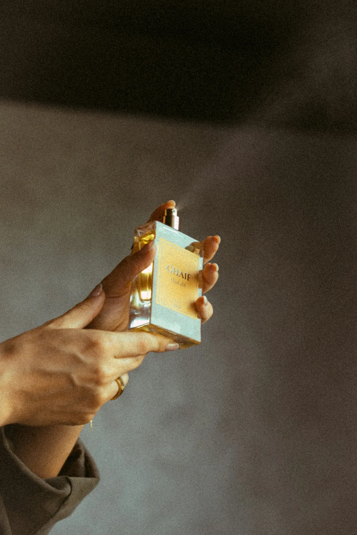 Hands holding and spraying a perfume bottle.